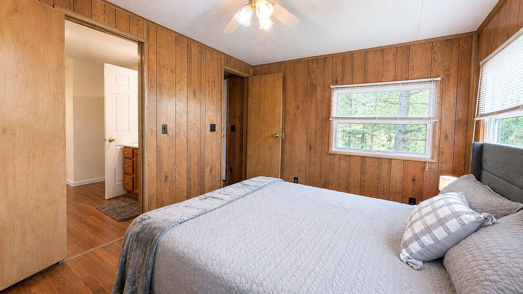 A bedroom with a bed, a window, wooden walls, and a door.