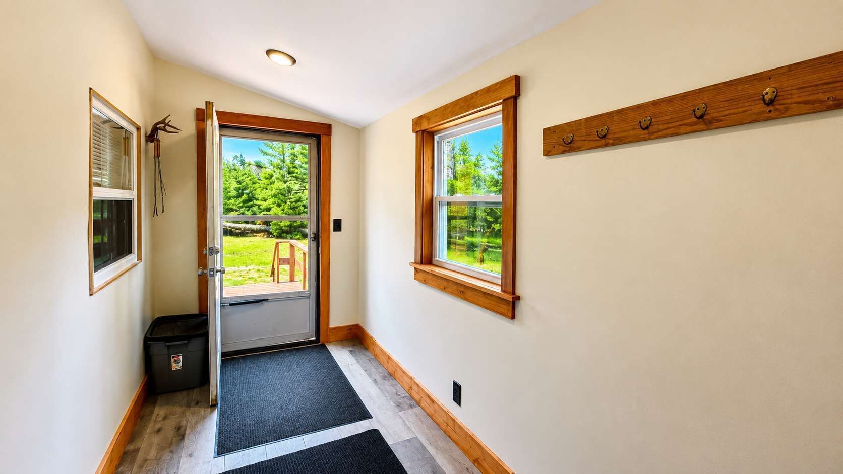 A hallway with a door leading to a deck, a window on the right, and a small trash bin.