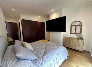 Ein Schlafzimmer mit einem Bett, einem an der Wand befestigten Fernseher, einem Kleiderschrank und einem Schrank.