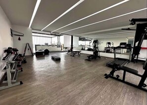 Ein geräumiger Fitnessraum mit unterschiedlichen Trainingsgeräten, einer Spiegelwand und einem Holzboden.