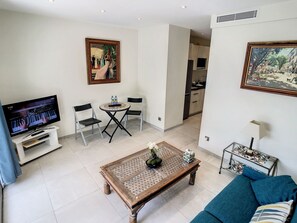 A living room with a television, a coffee table with a plant, a sofa, and a dining area with chairs and a table. - Apartment  by Interhome (Cannes)