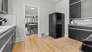 Une cuisine moderne avec un réfrigérateur noir, un plancher en bois et un coin repas à l’arrière-plan.