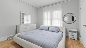 Une chambre à coucher avec un lit, une commode, un miroir et un petit placard.