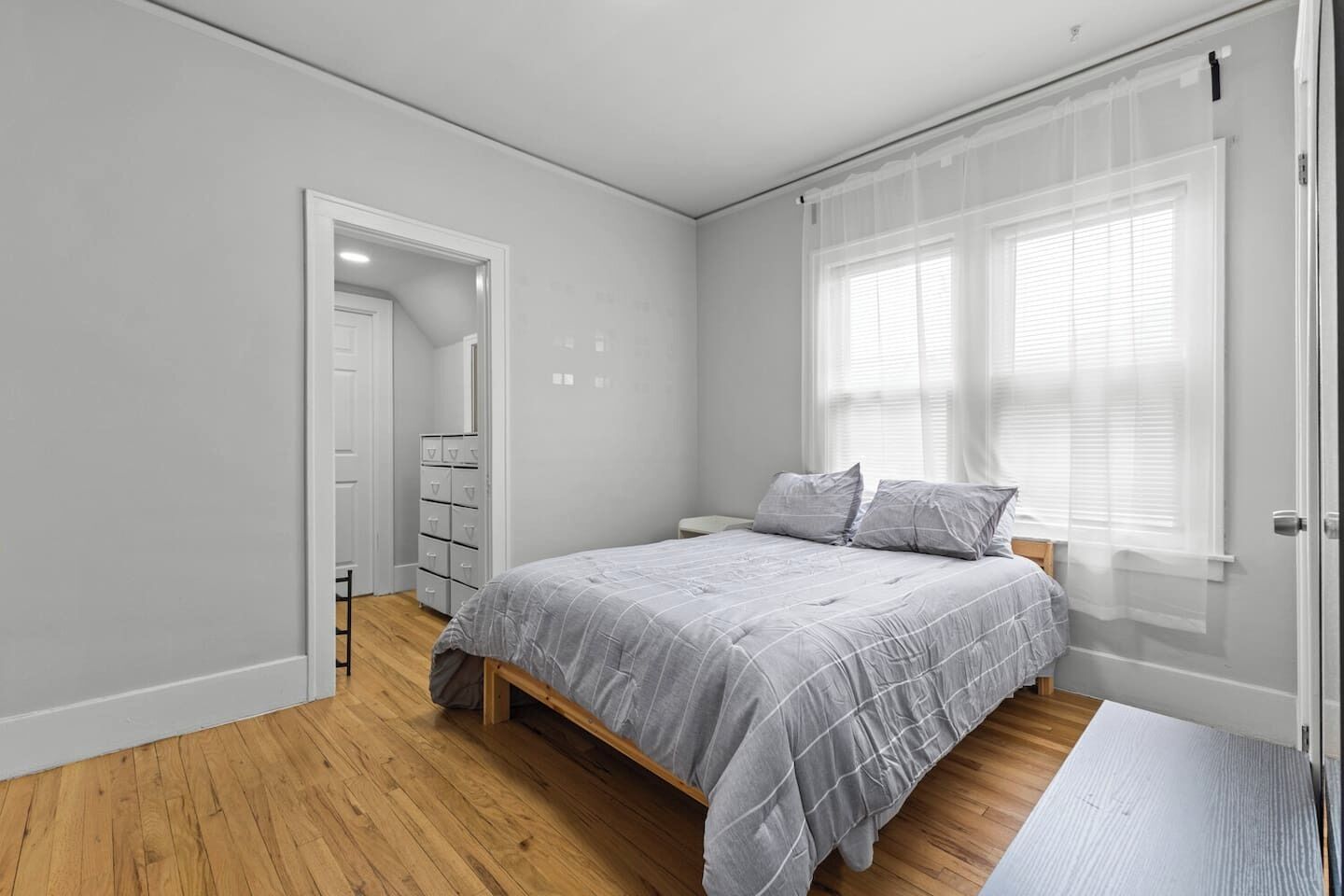 A bedroom with a bed, a wardrobe, a door, and a window with blinds.