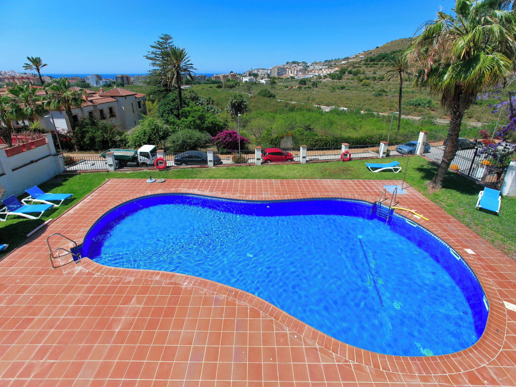 Une piscine dotée d’une terrasse carrelée, entourée de verdure et offrant une vue sur la mer.