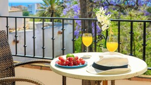 En balkon med et bord dækket til to, med en tallerken druer, en lime, to glas appelsinjuice og en hvid hat.