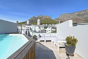 A rooftop pool with a white lounge area and a view of mountains.