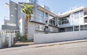 Un edificio moderno de varios pisos con balcones, ventanas amplias y una entrada protegida por una reja.