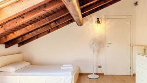 A bedroom with a sloped ceiling, a bed, a standing fan, a white door, and a dresser. - Legnone by Interhome (Sorico Albonico)
