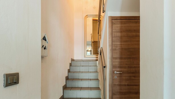 A staircase leading to a wooden door, with a light switch and a framed picture on the wall. - Legnone by Interhome (Sorico Albonico)