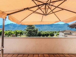 Ein Balkon mit großem Sonnenschirm, Blick auf Berge und ein Gebäude im Hintergrund.