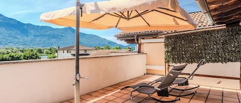 A rooftop terrace with a retractable awning, a lounge chair, and a view of mountains.