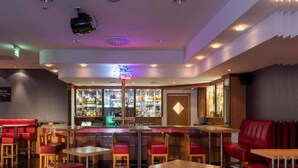 Angolo bar con sedute rosse, insegna al neon e bancone.