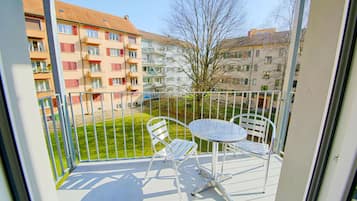 A balcony with a metal table and two chairs, overlooking a grassy area and buildings.