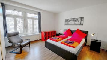 A modern bedroom with a bed, a chair, a nightstand, and a window.