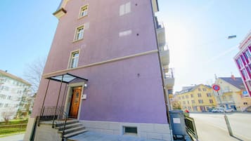 A multi-story building with a purple facade, a visible entrance with steps, and a small window on the ground floor.