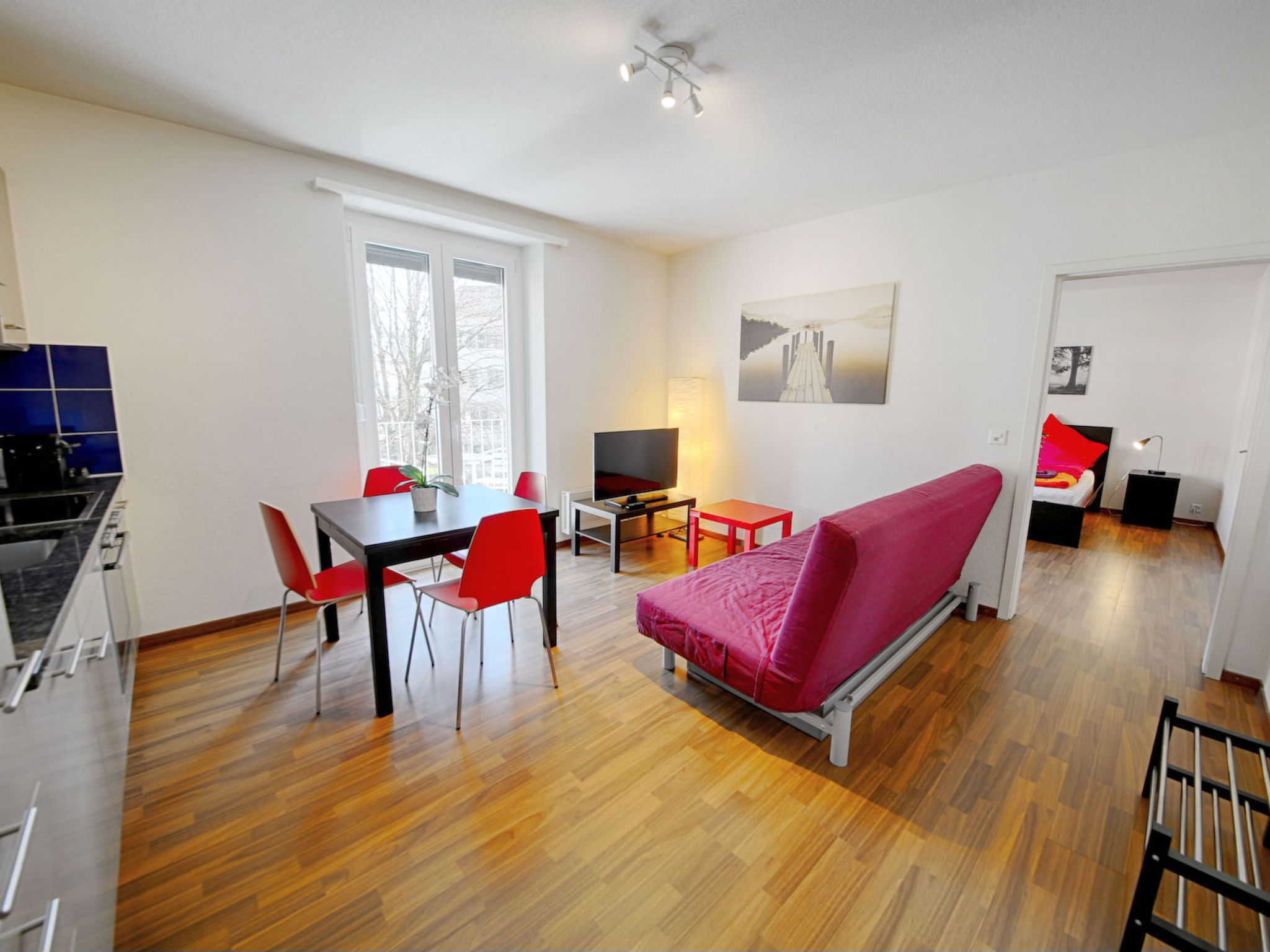 A modern living space with a dining area, a sofa, a TV, and a kitchen.