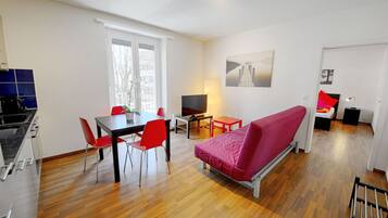 A modern living space with a dining area, a sofa, a TV, and a kitchen.
