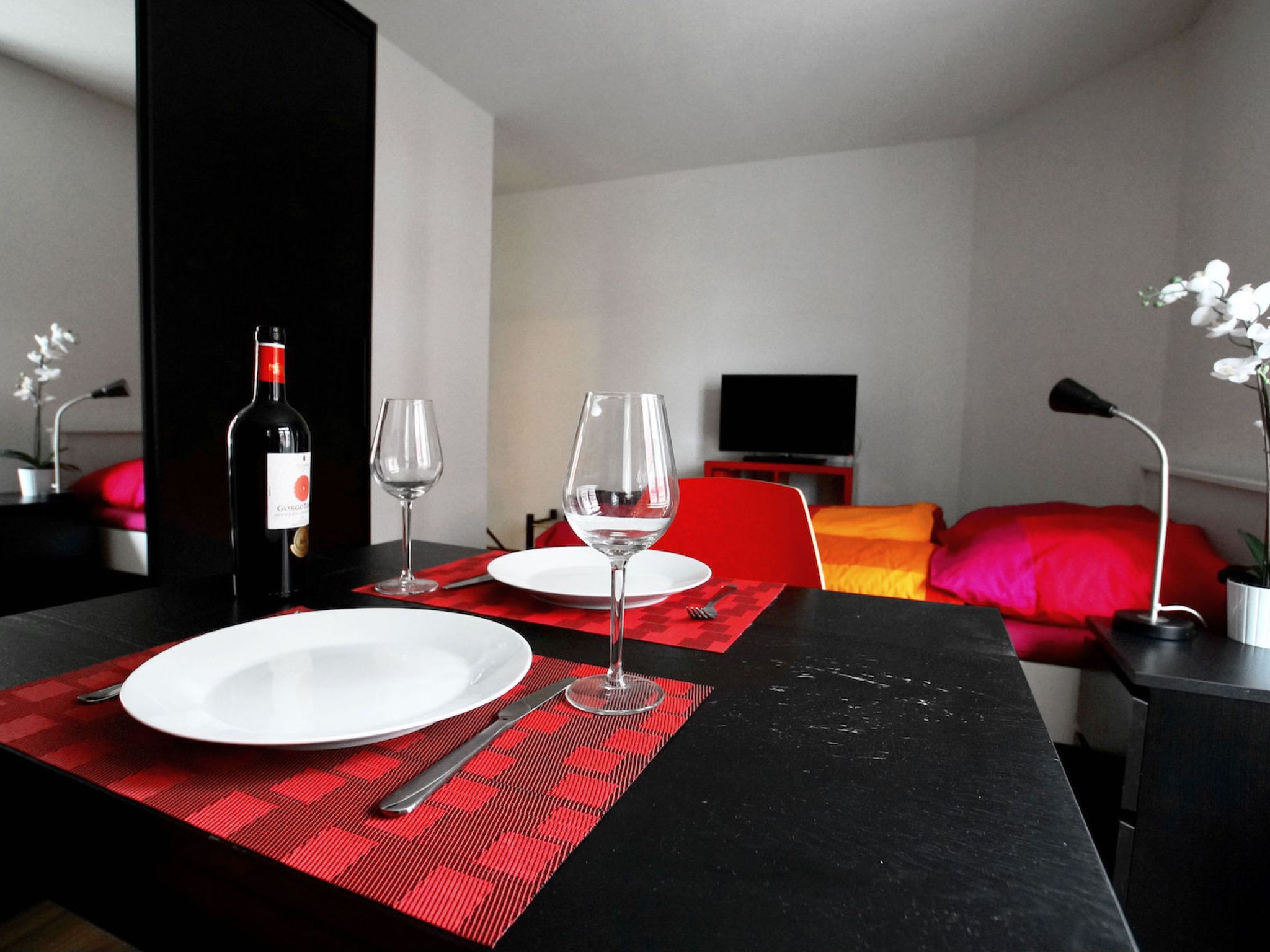 A dining area with a table set for two, a bottle of wine, and a glass.