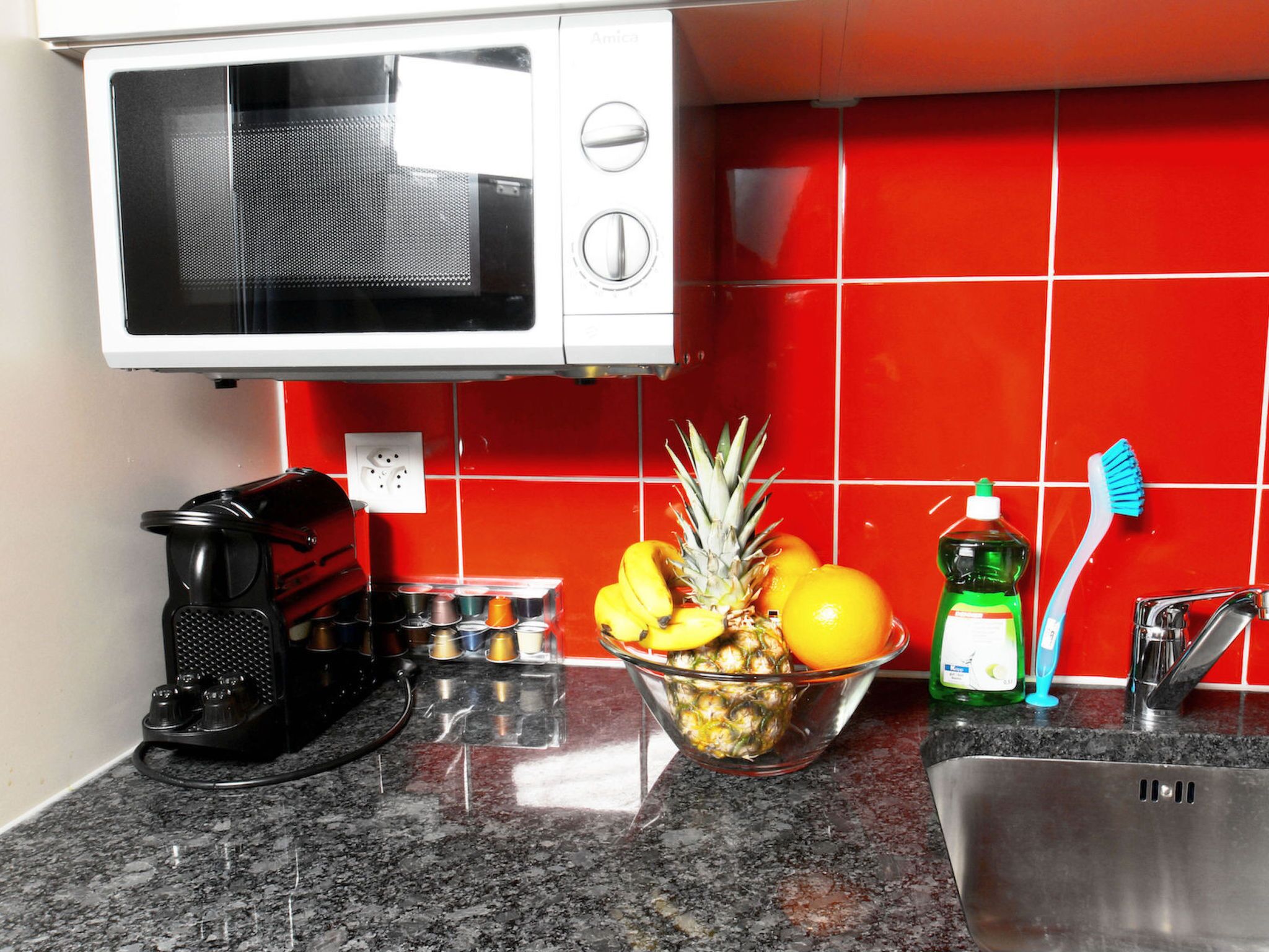 A kitchen with a microwave, a coffee maker, a bowl of fruit, and a sink.