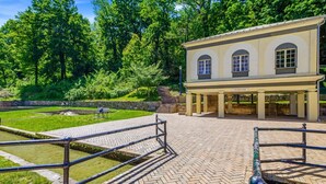 A historical building with arched windows, a paved walkway, and a surrounding garden. - Whimsical Haven By The Springs - Wifi | Walk to Everything (Berkeley Springs)