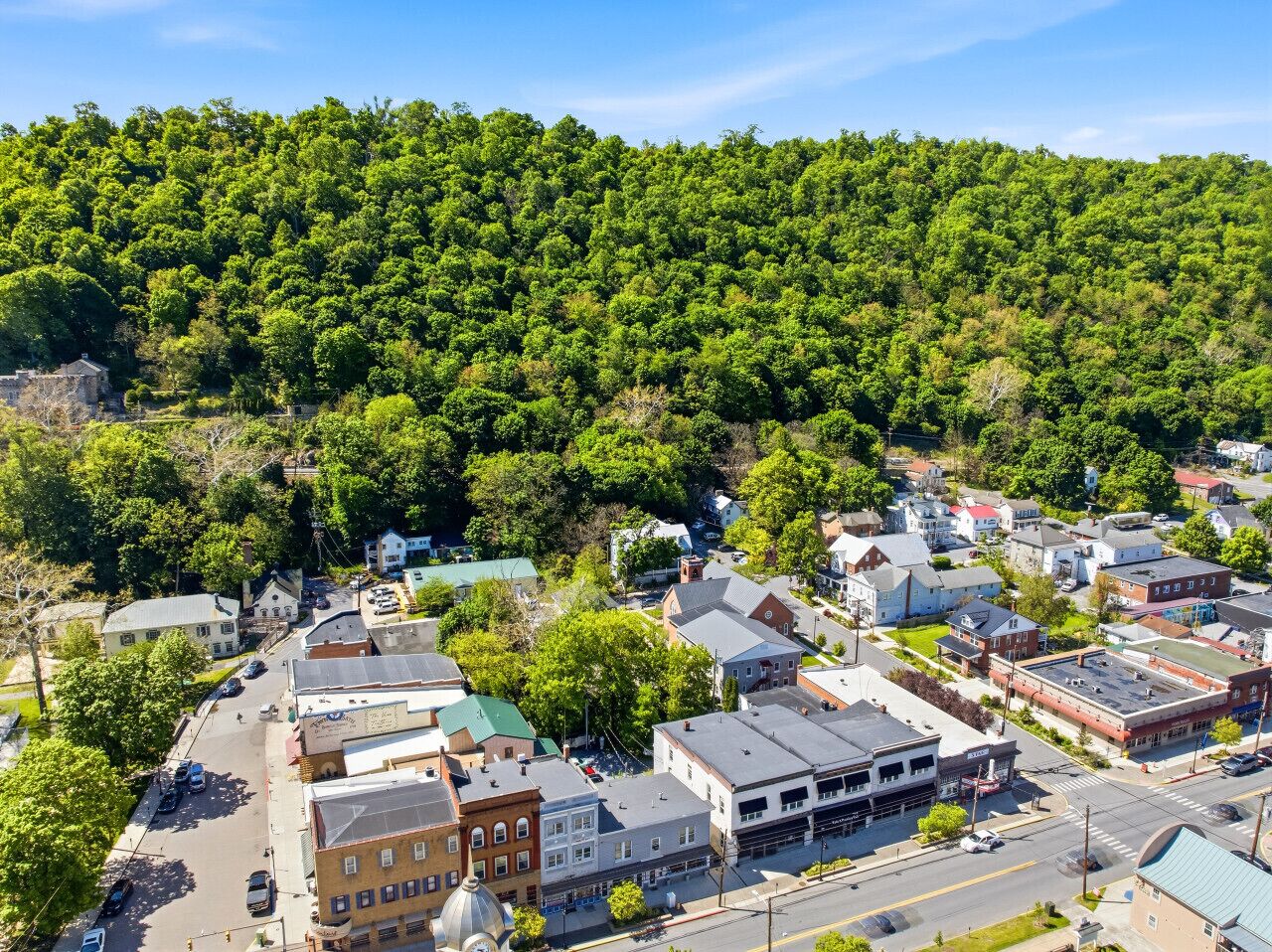 A town with a mix of residential and commercial buildings, a main street, and a hill with dense greenery in the background.