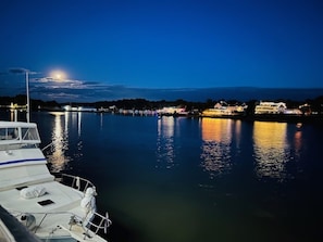 Blick auf das Wasser mit einem vertäuten Boot, ruhiger Wasserfläche und Gebäuden am Ufer.