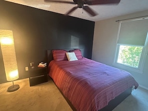 Ein Schlafzimmer mit Bett, Deckenventilator, Nachttisch, Lampe und Fenster.