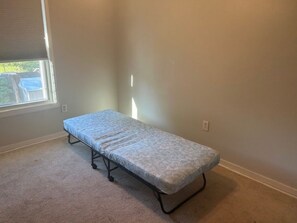 Ein kleines Zimmer mit einem Einzelbett, Fenster, Teppichboden und schlichten Wänden.