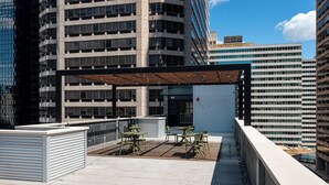 A rooftop terrace with outdoor seating, a covered area, and a view of surrounding high-rise buildings. - Sosuite | Deluxe Queen Room w Desk (Philadelphia)