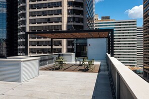 A rooftop terrace with outdoor seating, a covered area, and a view of surrounding high-rise buildings. - Sosuite | Deluxe Queen Room w Desk (Philadelphia)