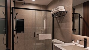 A modern bathroom with a glass-enclosed shower, a toilet, a sink, and a towel rack. - Sosuite | Deluxe Queen Room w Desk (Philadelphia)