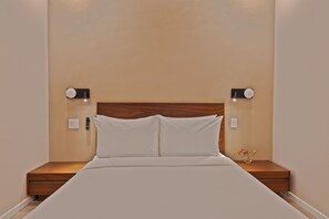 A neatly made bed with a wooden headboard, two bedside tables with lamps, and a wall-mounted light fixture.