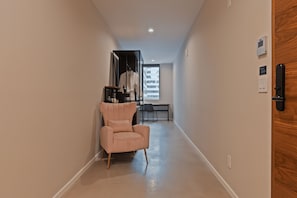 A hallway with a chair, a coat rack, a desk, and a window.