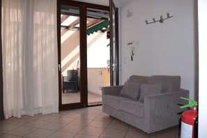 A living room with a sofa, a sliding glass door leading to an outdoor area, and a fire extinguisher. - Balcony, Lake View, Walking Distance Lazise Centre (Lazise)
