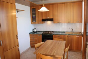 A kitchen with wooden cabinets, a granite countertop, a gas stove, and a dining table with chairs. - Balcony, Lake View, Walking Distance Lazise Centre (Lazise)
