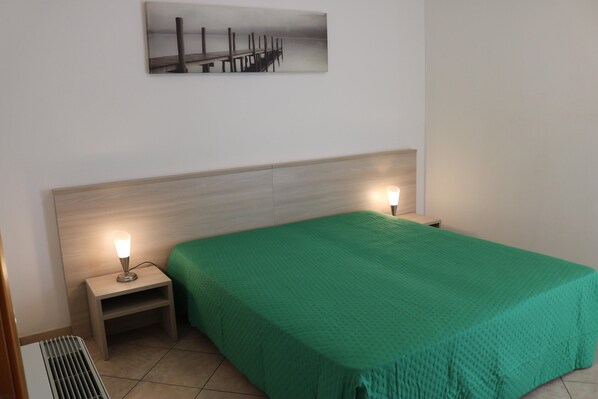 A hotel room with a bed, two bedside lamps, a nightstand, a radiator, and a painting on the wall. - Balcony, Lake View, Walking Distance Lazise Centre (Lazise)