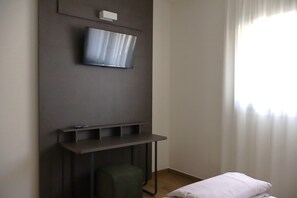A hotel room with a flat-screen TV mounted on the wall, a small table, a green chair, and a bed with white bedding. - In a Residence, Air-conditioned, Large Outdoor Space (Marone)