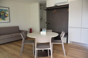 A modern living room with a sofa, a round table with chairs, a kitchen area with cabinets, and a fire extinguisher. - In a Residence, Air-conditioned, Large Outdoor Space (Marone)