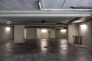 A spacious parking garage with concrete pillars, overhead pipes, and fluorescent lighting. - In a Residence, Air-conditioned, Large Outdoor Space (Marone)