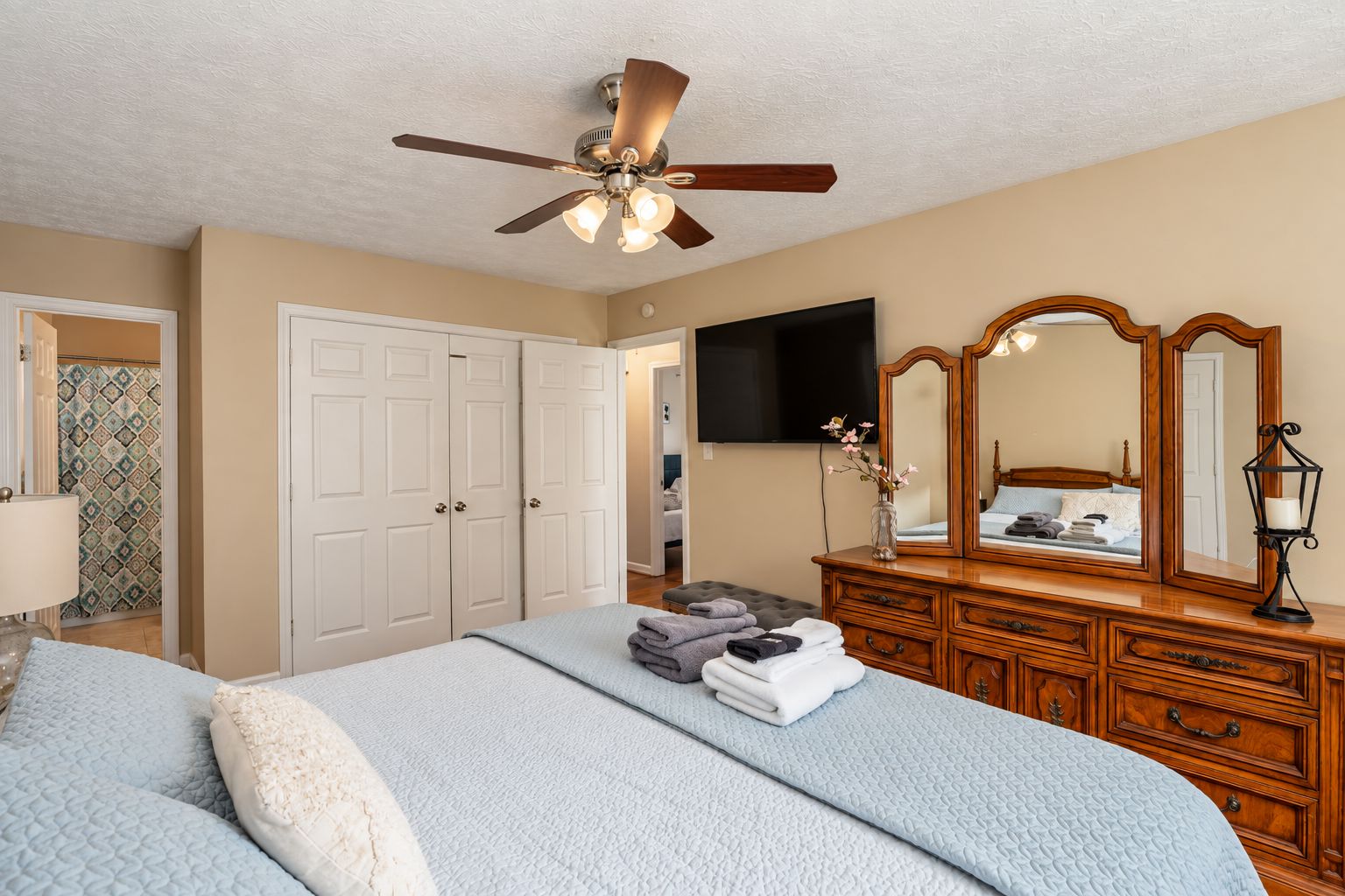 A bedroom with a bed, a dresser, a ceiling fan, a television, and a mirror.