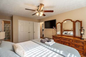 A bedroom with a bed, dresser, mirror, ceiling fan, and a TV on the wall. - Peachtree City Home Near Lake with Yard & Firepit (Peachtree City)