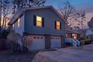 A two-story house with a garage, a covered porch, and a stone foundation. - Peachtree City Home Near Lake with Yard & Firepit (Peachtree City)