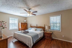 A bedroom with a bed, wooden nightstands, a ceiling fan, and two windows with blinds. - Peachtree City Home Near Lake with Yard & Firepit (Peachtree City)