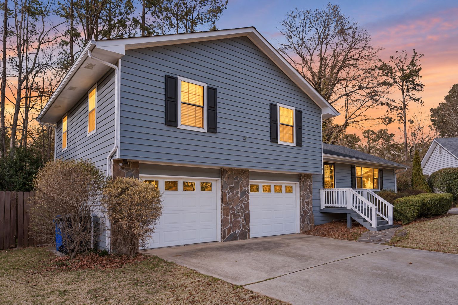 A two-story house with a stone foundation, a garage, and a front porch with a staircase.
