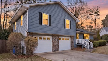 A two-story house with a stone foundation, a garage, and a front porch with a staircase.