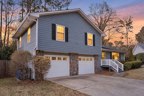 A two-story house with a stone foundation, a garage, and a front porch with a staircase. - Peachtree City Home Near Lake with Yard & Firepit (Peachtree City)