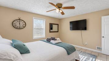 Une chambre à coucher avec un lit, un ventilateur de plafond, une horloge, une fenêtre, un téléviseur et une porte.