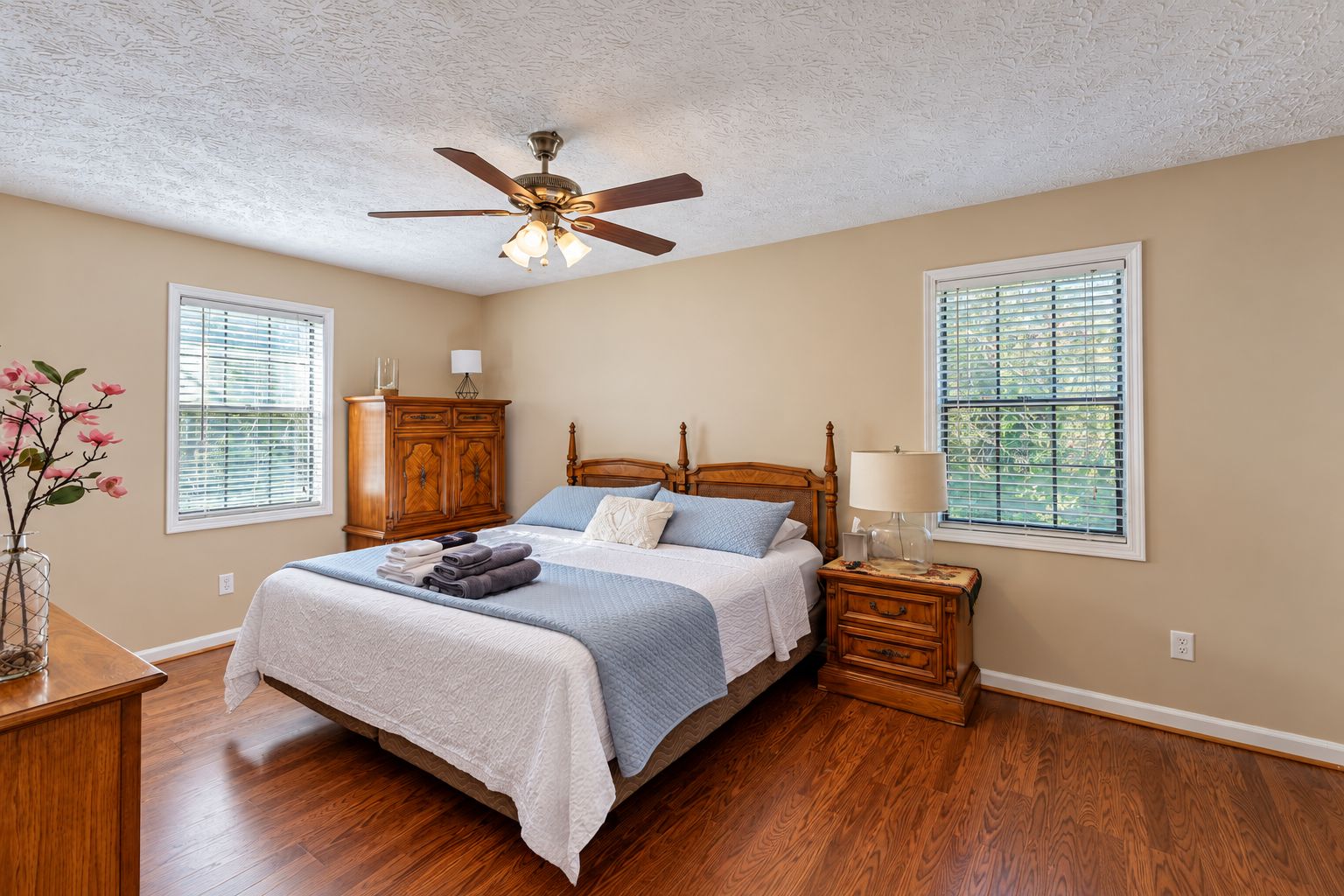 A bedroom with a wooden bed, a ceiling fan, and two windows with blinds.