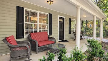 A covered porch with wicker furniture, a glass table, and a black door.